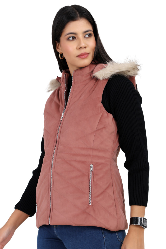 A standing side pose of a woman wearing Coatsnmore’s half sleeves jacket in onion pink colour with a textured pattern, removable hood with faux fur trim, side zippered pockets, a zip closure and blue jeans.